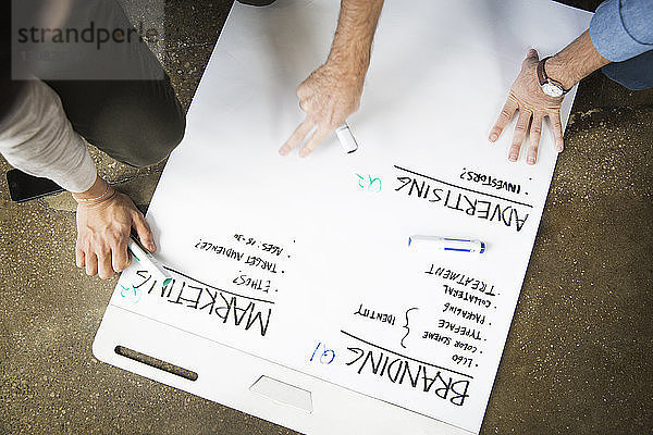 Ausgeschnittenes Bild von Geschäftsleuten  die in einem kreativen Büro an einer weißen Tafel schreiben
