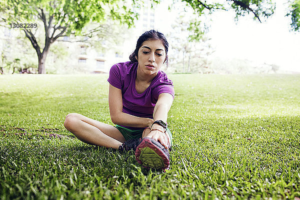 Entschlossene Sportlerin berührt die Zehen  während sie im Park auf Gras sitzt