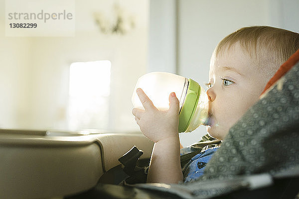 Nahaufnahme eines kleinen Jungen  der Milch trinkt  während er zu Hause auf einem Hochstuhl sitzt