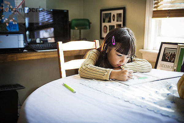 Mädchen zeichnet auf Buch  während sie am Tisch sitzt