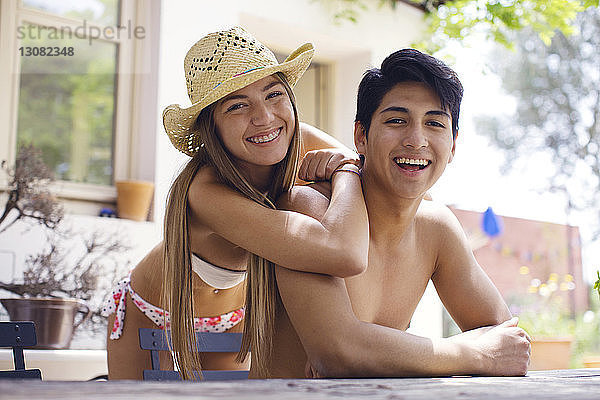 Porträt einer glücklichen Frau im Bikini  die sich an einen am Tisch sitzenden Mann ohne Hemd lehnt