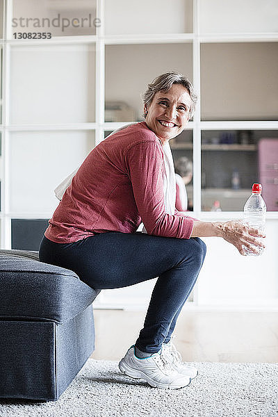 Seitenansicht Porträt einer glücklichen reifen Frau  die zu Hause auf dem Sofa sitzend eine Wasserflasche hält
