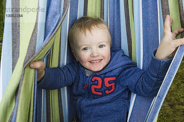 Portrait eines fröhlichen Jungen  der in einer Hängematte im Hinterhof liegt