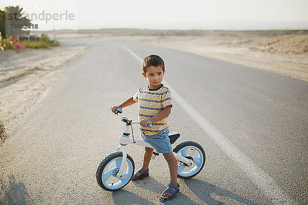 Junge in voller Länge mit Fahrrad  der auf der Landstraße stehend wegschaut