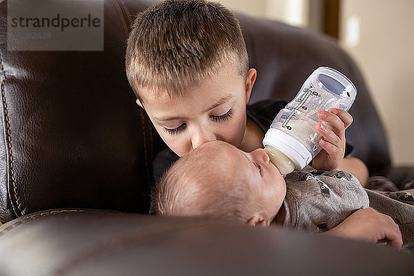 Junge gibt seinem Bruder Milch aus der Babyflasche  während er ihn zu Hause küsst