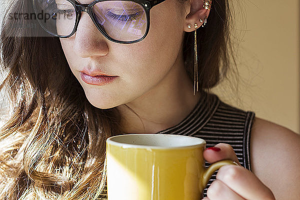 Nahaufnahme einer nachdenklichen Frau mit Brille  die zu Hause einen Becher hält