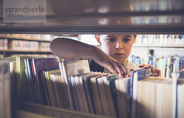 Ernsthafter Junge sucht Buch aus dem Regal in der Bibliothek