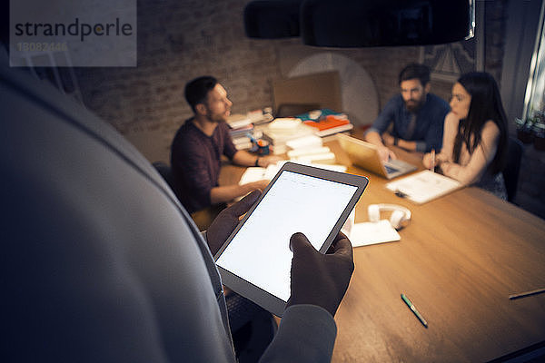 Ausgeschnittenes Bild eines Geschäftsmannes  der einen Tablet-Computer benutzt  während seine Kollegen im Hintergrund diskutieren