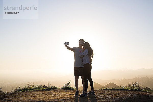 Pärchen  das sich durch ein Smartphone selbstständig macht  während es auf einem Berg vor klarem Himmel steht