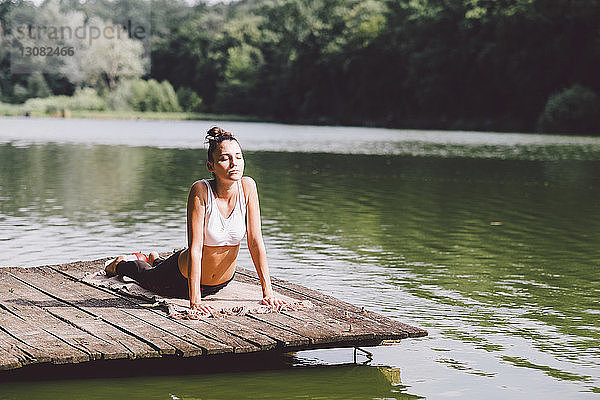 Frau übt Kobra-Pose am Pier über einem See im Wald