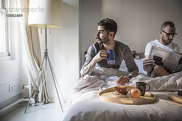 Schwuler Mann beim Frühstück  während der Partner zu Hause im Bett Zeitung liest