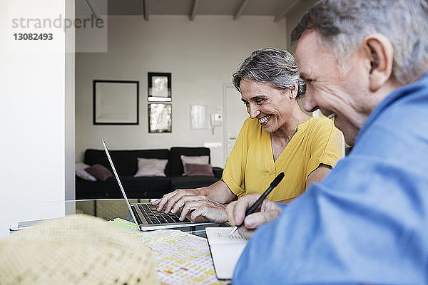 Fröhliches älteres Ehepaar mit Laptop bei der Urlaubsplanung zu Hause