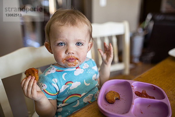 Porträt eines süßen Mädchens  das zu Hause am Tisch sitzend Nahrung zu sich nimmt