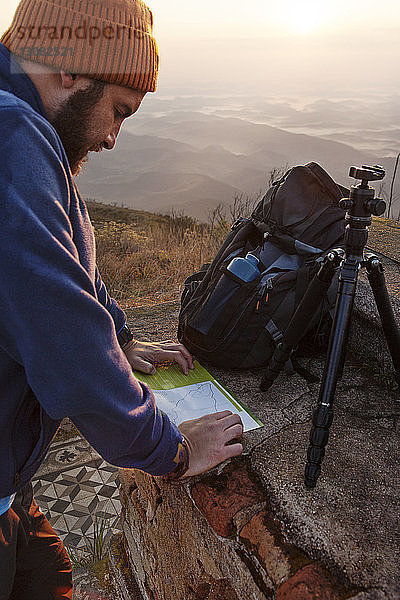 Mann schaut auf Karte  während er bei Sonnenuntergang auf einem Berg steht