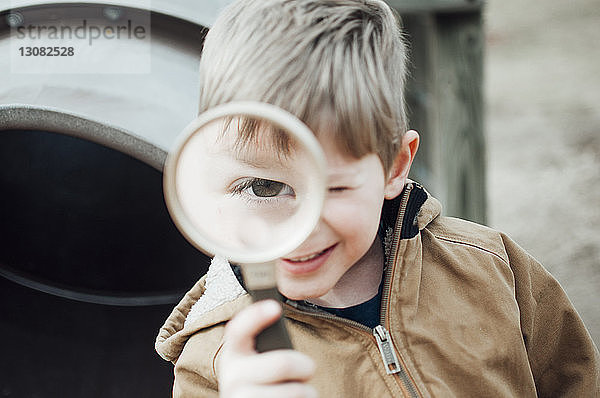 Nahaufnahme eines glücklichen Jungen  der mit der Lupe auf dem Spielplatz spielt