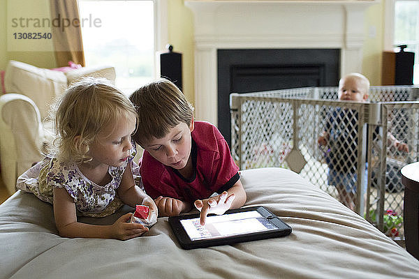 Kleiner Junge schaut Geschwistern am Tablet-Computer zu  während er in der Krippe steht