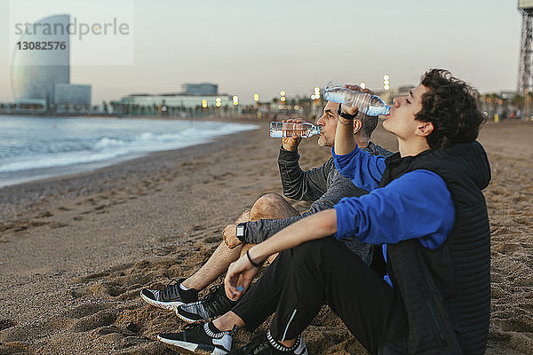 Vater und Sohn trinken Wasser  während sie gegen das Hotel Vela am Strand sitzen