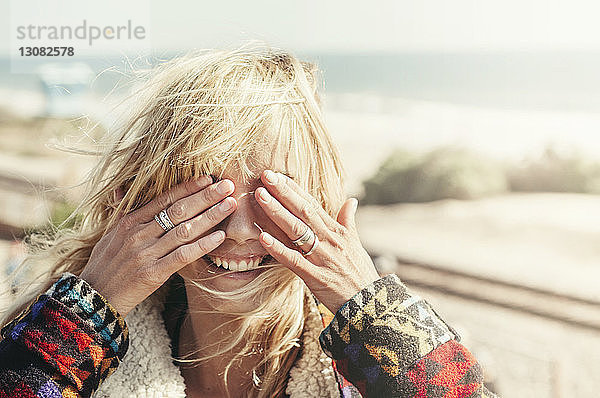 Glückliche junge Frau bedeckt Augen am Strand