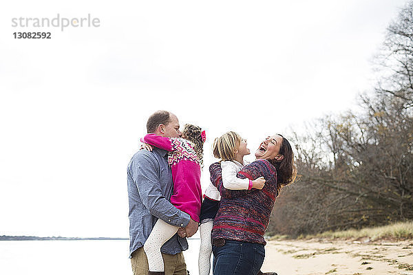 Glückliche Eltern  die ihre Töchter am Strand vor klarem Himmel umarmen