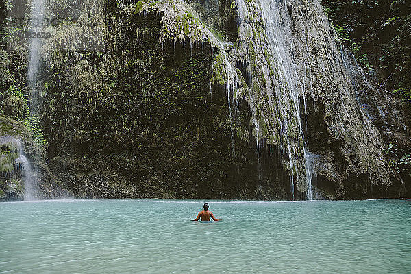 Rückansicht eines Mannes ohne Hemd  der im Fluss am Wasserfall im Wald schwimmt