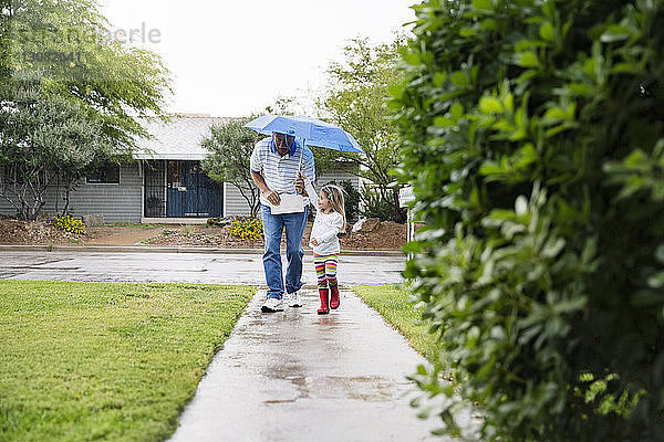Grossvater und Enkelin spazieren unter einem Regenschirm auf einem Fussweg im Park