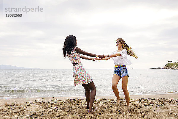 Fröhliche Freundinnen spielen Ring-um-den-Rosen am Strand