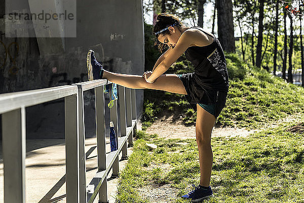 Seitenansicht einer Athletin  die ihr Bein auf einem Geländer im Park streckt