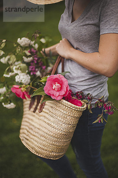 Mittelteil einer Frau  die einen Korb mit Blumen trägt