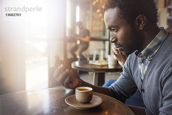 Nachdenklicher Mann hält Handy in der Hand  während er im Café am Tisch sitzt