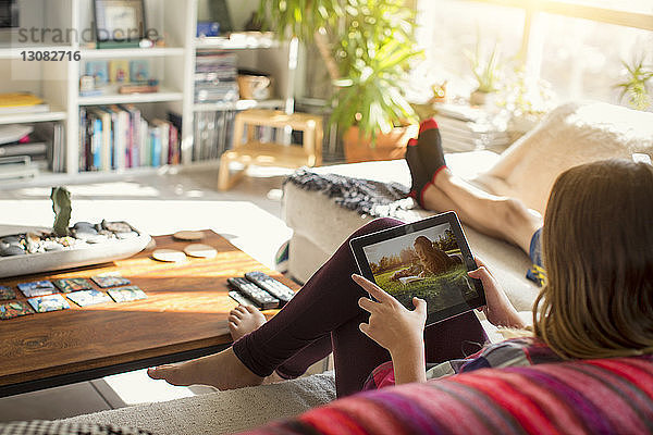 Mädchen betrachtet Bilder im Tablet-Computer  während sie auf dem Sofa sitzt