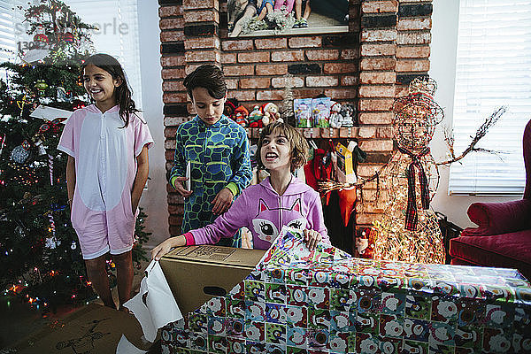 Glückliche Geschwister öffnen Weihnachtsgeschenk zu Hause an einer Ziegelmauer