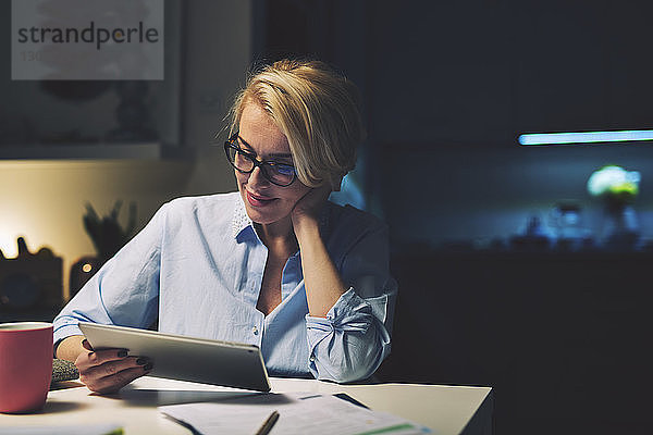 Lächelnde Geschäftsfrau mit Tablet-Computer am Schreibtisch im Heimbüro
