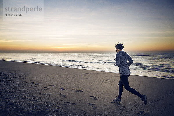 Frau joggt am Strand gegen den Himmel