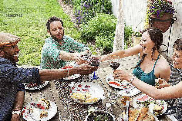 Schrägansicht von Freunden  die am Tisch im Hof sitzen und auf Weingläser anstoßen