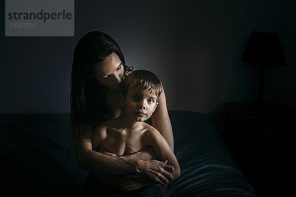 Porträt eines Jungen mit zu Hause auf dem Bett sitzender Mutter