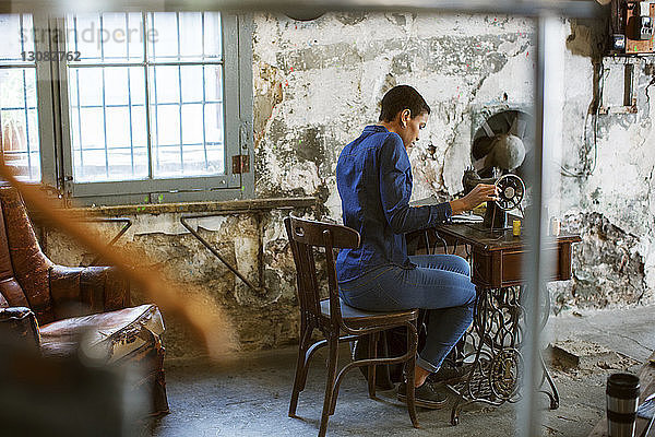 Modedesignerin arbeitet in alter Werkstatt an einer Nähmaschine