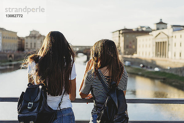 Rückansicht von Freunden mit Rucksäcken  die auf der Brücke über den Arno vor klarem Himmel in der Stadt stehen