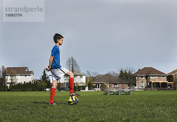 Seitenansicht eines Jungen mit Fussball  der auf einem Rasenfeld steht