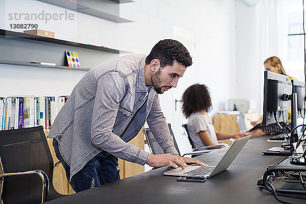 Geschäftsmann benutzt Laptop-Computer mit weiblichen Kollegen im Hintergrund im Büro