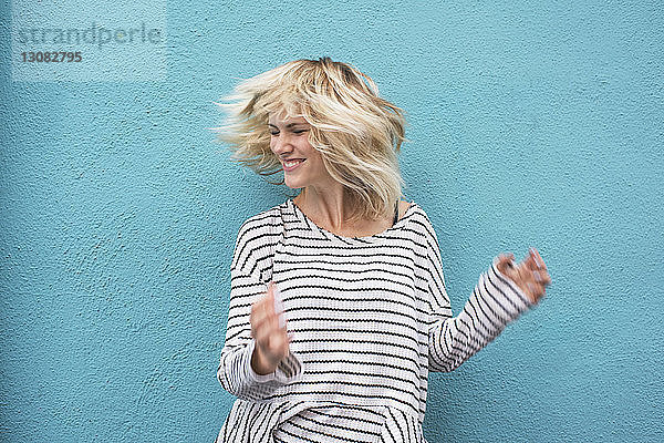 Fröhliche junge Frau wirft Haare gegen blaue Wand