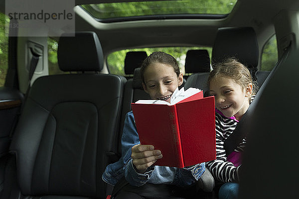 Glückliche Schwestern lesen Buch  während sie im Auto sitzen