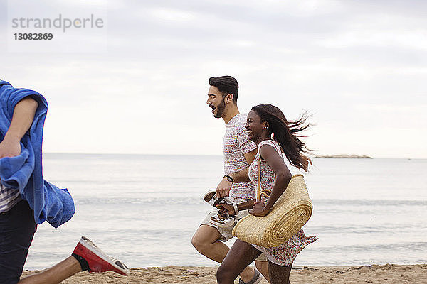 Seitenansicht von fröhlichen multiethnischen Freunden  die am Strand an Land laufen