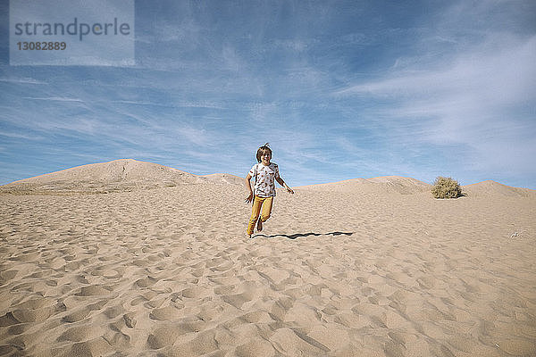 Verspielter Junge rennt am sonnigen Tag in der Wüste gegen bewölkten Himmel