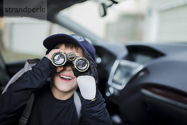 Nahaufnahme eines Jungen  der im Auto sitzend durch ein Fernglas schaut