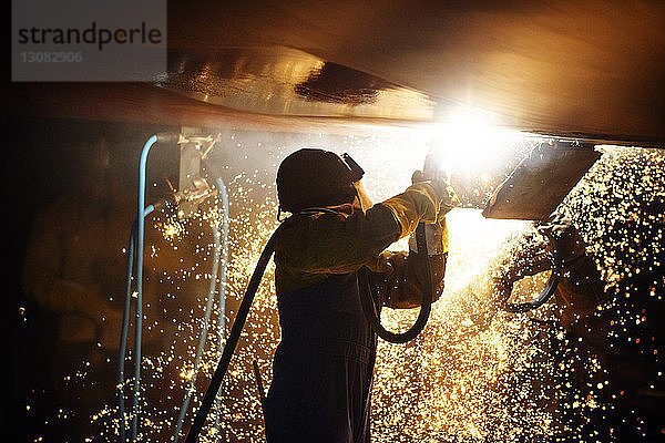 Seitenansicht eines Arbeiters beim Schweißen eines Flugzeugflügels bei Nacht