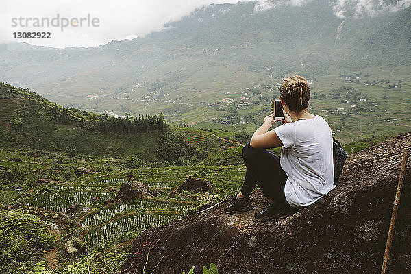 Rückansicht einer Frau  die Landschaft mit einem Smartphone fotografiert