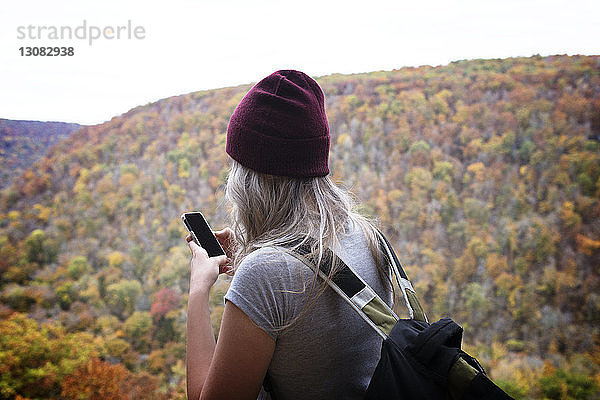 Rückansicht einer jungen Frau  die telefoniert  während sie am Berg steht
