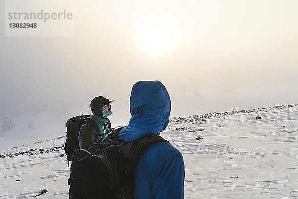 Männliche Freunde stehen bei nebligem Wetter auf schneebedecktem Feld