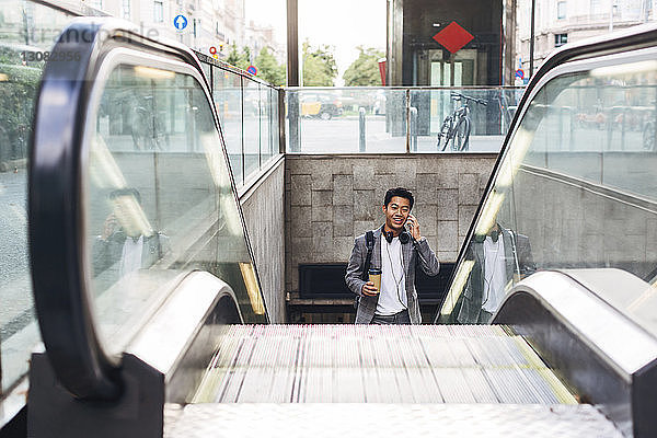 Geschäftsmann spricht am Smartphone  während er auf der Rolltreppe steht