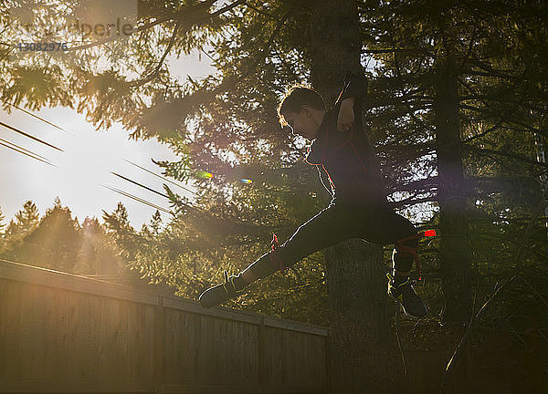 Junge in voller Länge  der bei Sonnenuntergang im Garten gegen einen Baum springt